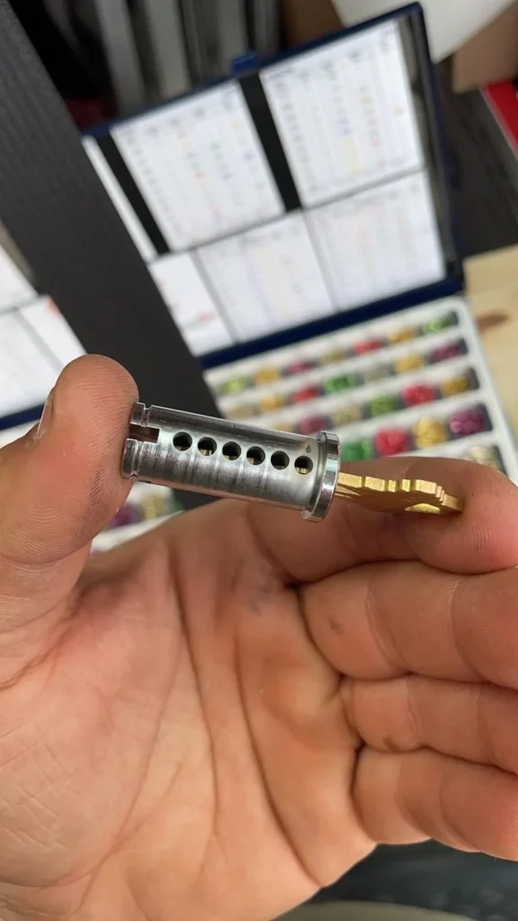 Lock cylinder with visible pin chambers next to its key, held in hand in Philadelphia